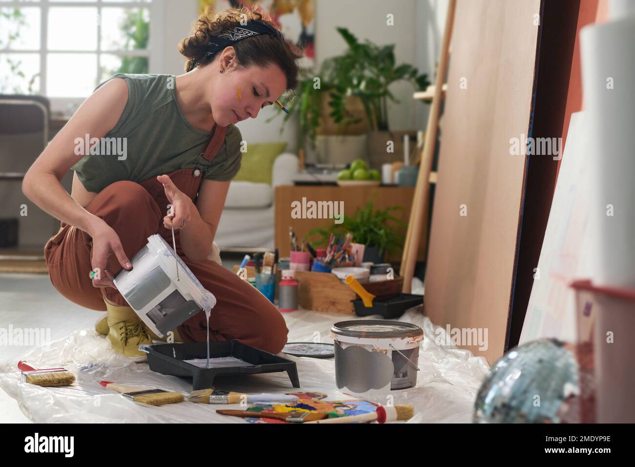Junge kreative Künstlerin gießt flüssige Farbe in die Plastikschale, bevor sie an der Gestaltung eines neuen Meisterwerks im Heimstudio arbeitet Stockfoto