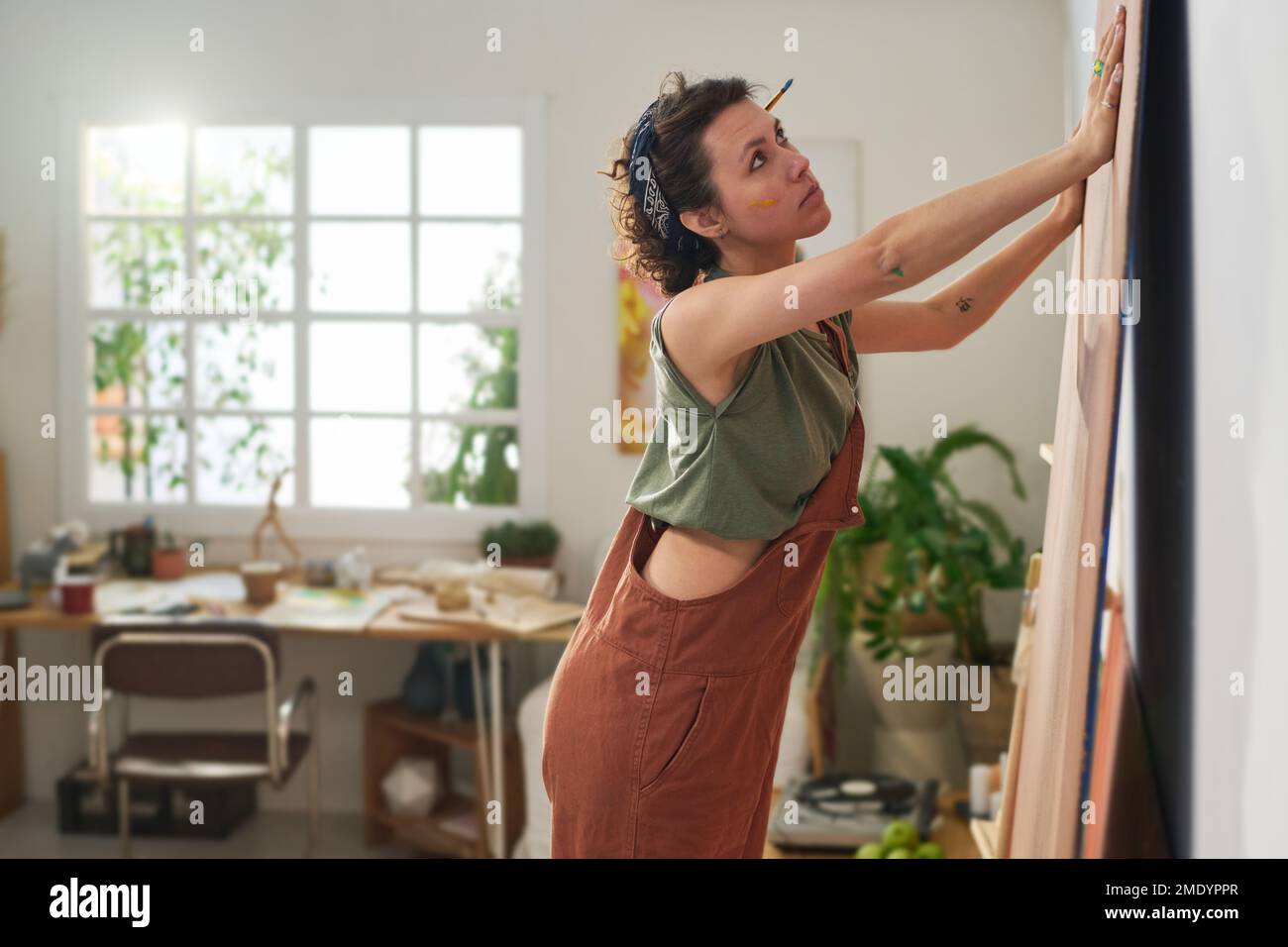 Junge kreative Malerin in Freizeitkleidung, die vor der Wand des Heimstudios steht und ein Panel für die Gestaltung neuer Kunstwerke vorbereitet Stockfoto