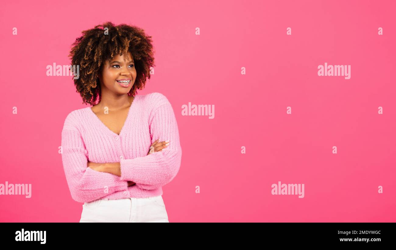 Fröhliche, afroamerikanische, lockige Dame mit gekreuzten Armen, die auf leeren Raum blickt Stockfoto