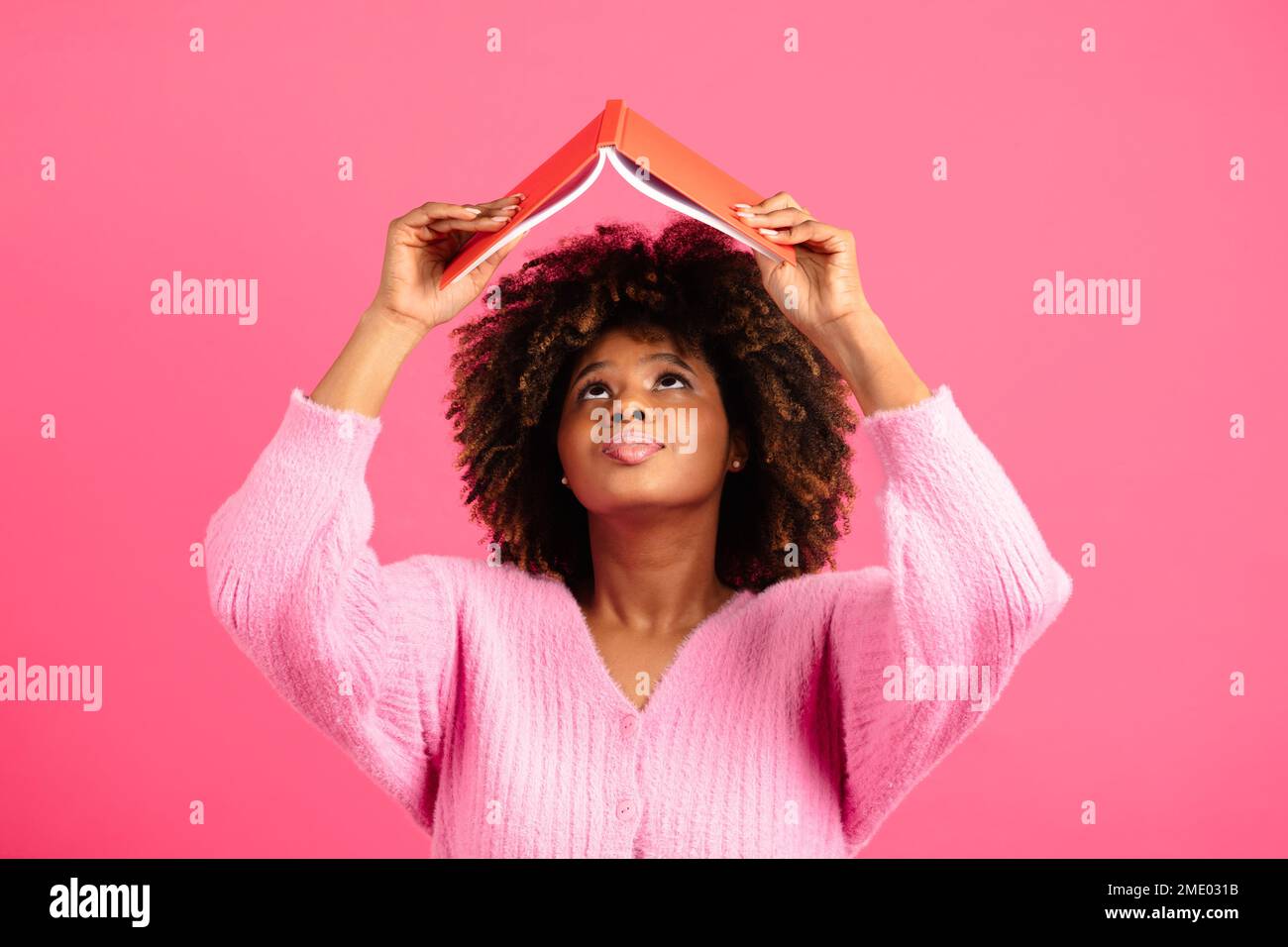 Eine ernsthafte, afroamerikanische Studentin mit lockigem Aufzug, die Tagebuch liest, nachsieht Stockfoto