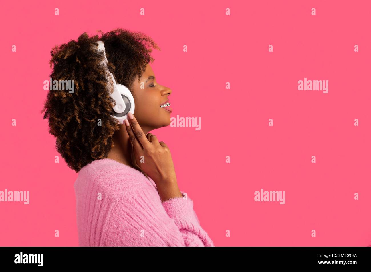 Lächelnde junge afroamerikanische lockige Frau mit Zahnspangen und geschlossenen Augen in kabellosen Kopfhörern genießen Musik Stockfoto
