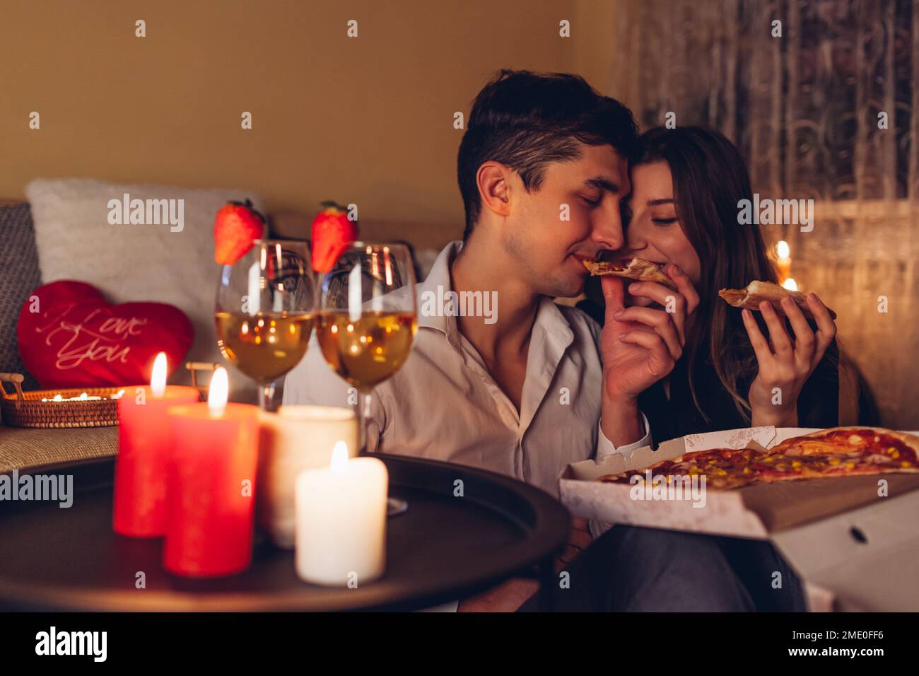 Valentinstagspaar, das Pizza isst, Champagner trinkt, ein romantisches Abendessen zu Hause feiert Stockfoto