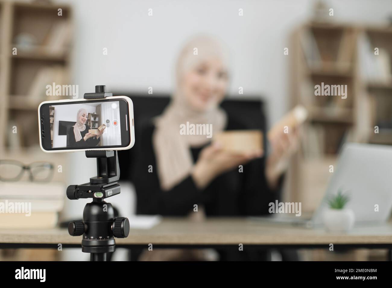 Konzentrieren Sie sich auf das Telefon einer glücklichen muslimischen Bloggerin, die Geschenkboxen von Unternehmen auspackt und Live-Streaming durchführt. Arabische Frau, die Smartphone-Kamera benutzt, um Inhalte zu erstellen. Stockfoto