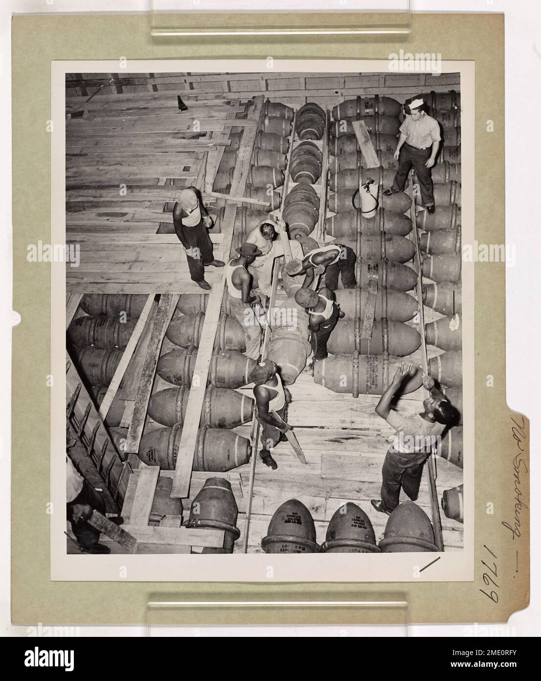 Die US Coast Guardsmen stehen mit Feuerlöschern in Alarmbereitschaft, während der Laderaum eines Handelsschiffes mit 1.000-Pfund-Luftbomben beladen ist. Die Wachleute sorgen für Sicherheit bei Gefahrguteinsätzen und betonen die Rolle der Küstenwache beim Umgang mit gefährlichen Materialien. Stockfoto