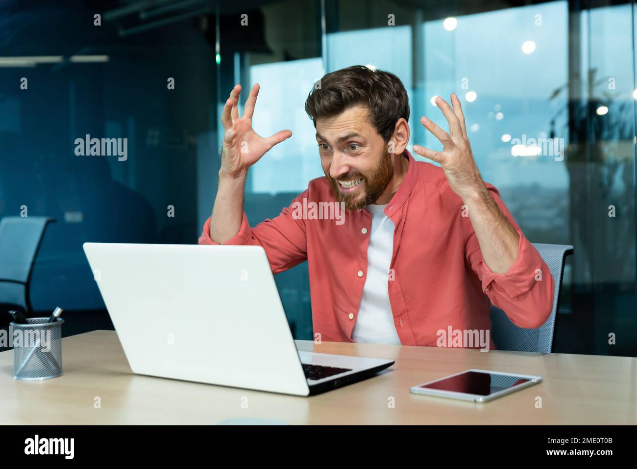 Wütender und nervöser Geschäftsmann, der per Fernzugriff per Videoanruf telefoniert, Mann, der Kollegen online anschreit, Chef im Hemd, der in einem modernen Büro mit einem Laptop arbeitet. Stockfoto