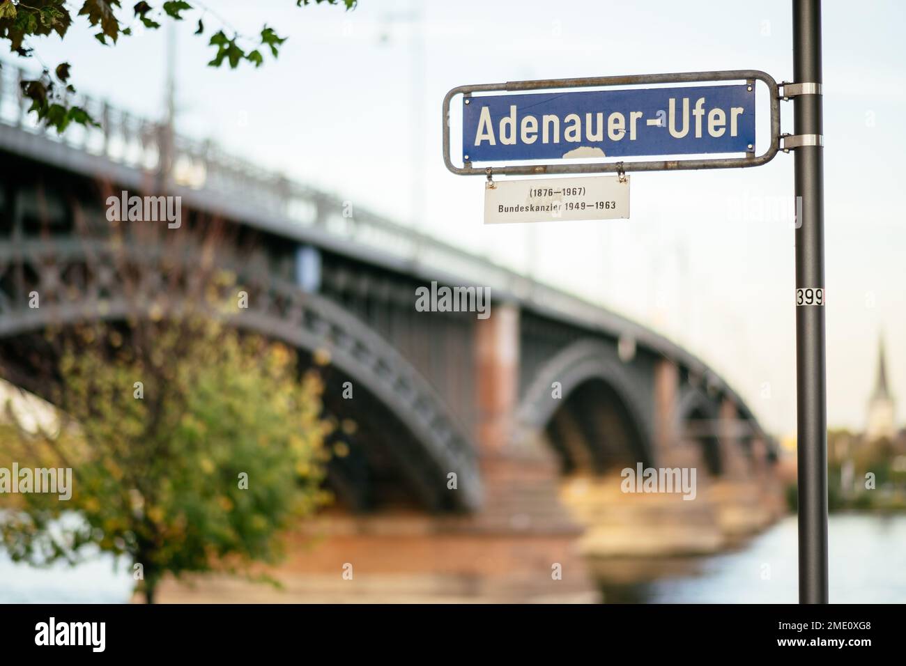 Das deutsche Straßenschild mit der Aufschrift Adenauer Ufer und der Theodor-Heuss-Brücke im Hintergrund Stockfoto
