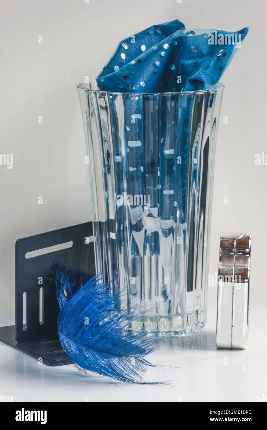 Sehen Sie raffinierte Gegenstände aus dem Büro in Silber, Blau und Schwarz. Vertikale Linien, blaue Feder und Stoff in Kontrastfarbe mit großer, geriffelter Glasvase. Stockfoto