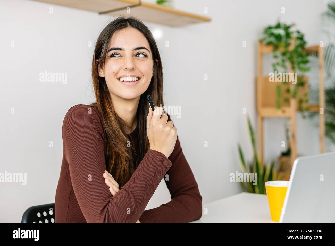 Junge, lächelnde, hübsche Geschäftsfrau, die mit einem Laptop an einem Tisch im Heimbüro sitzt Stockfoto