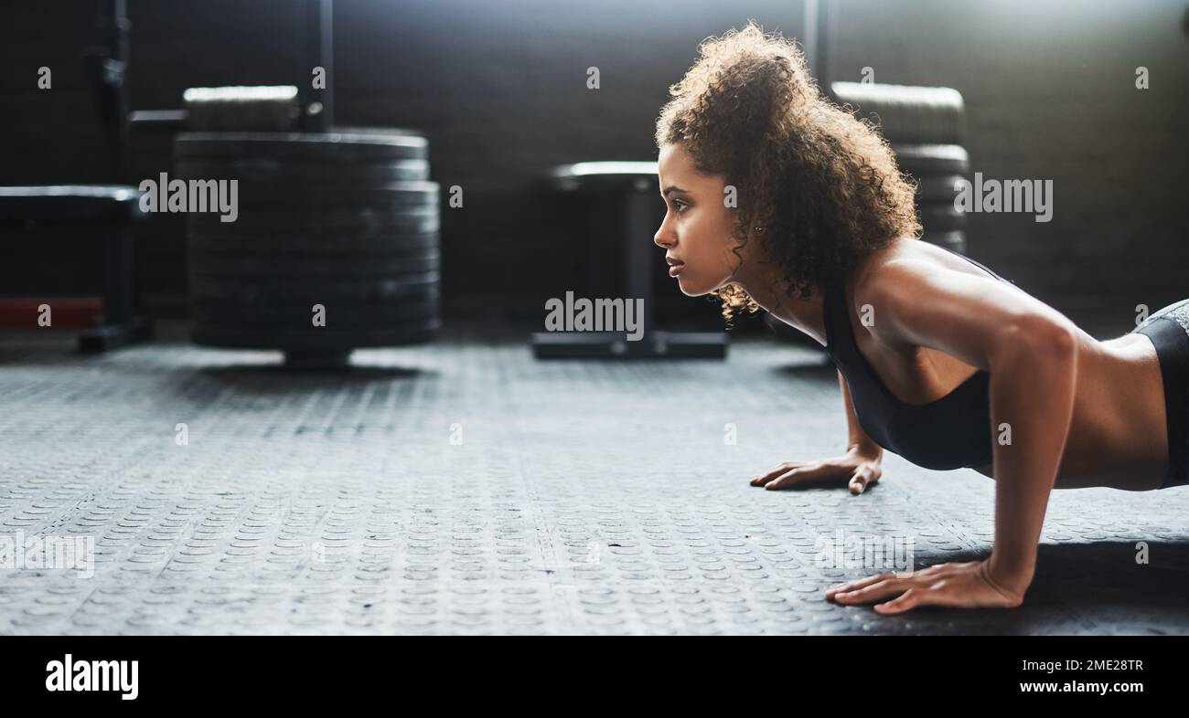 Steigere dich zu Größe. Eine junge Frau, die Liegestütze in einem Fitnessstudio macht. Stockfoto