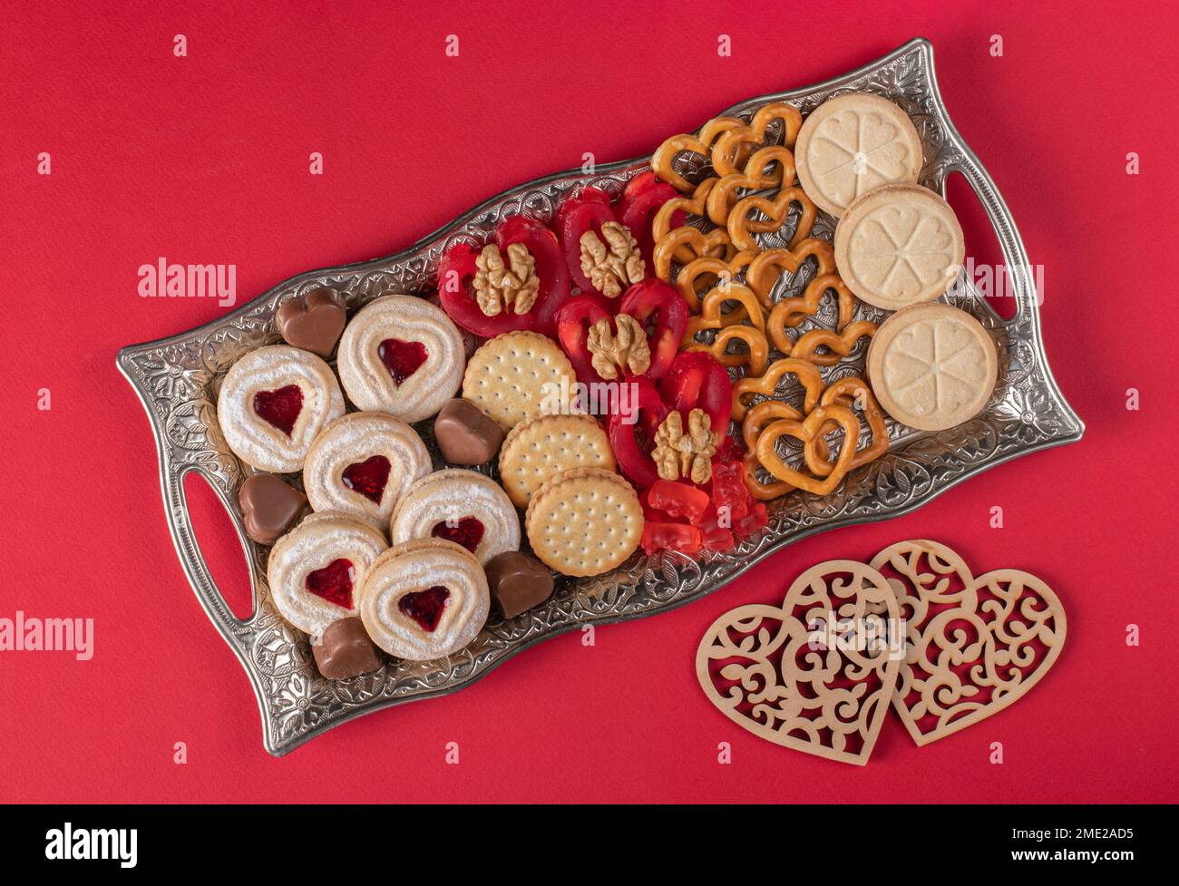 Valentinstag-Teller mit Shortbread, Schokoladenherzen, Crackern, roten Süßigkeiten und Walnüssen auf rotem Hintergrund Stockfoto