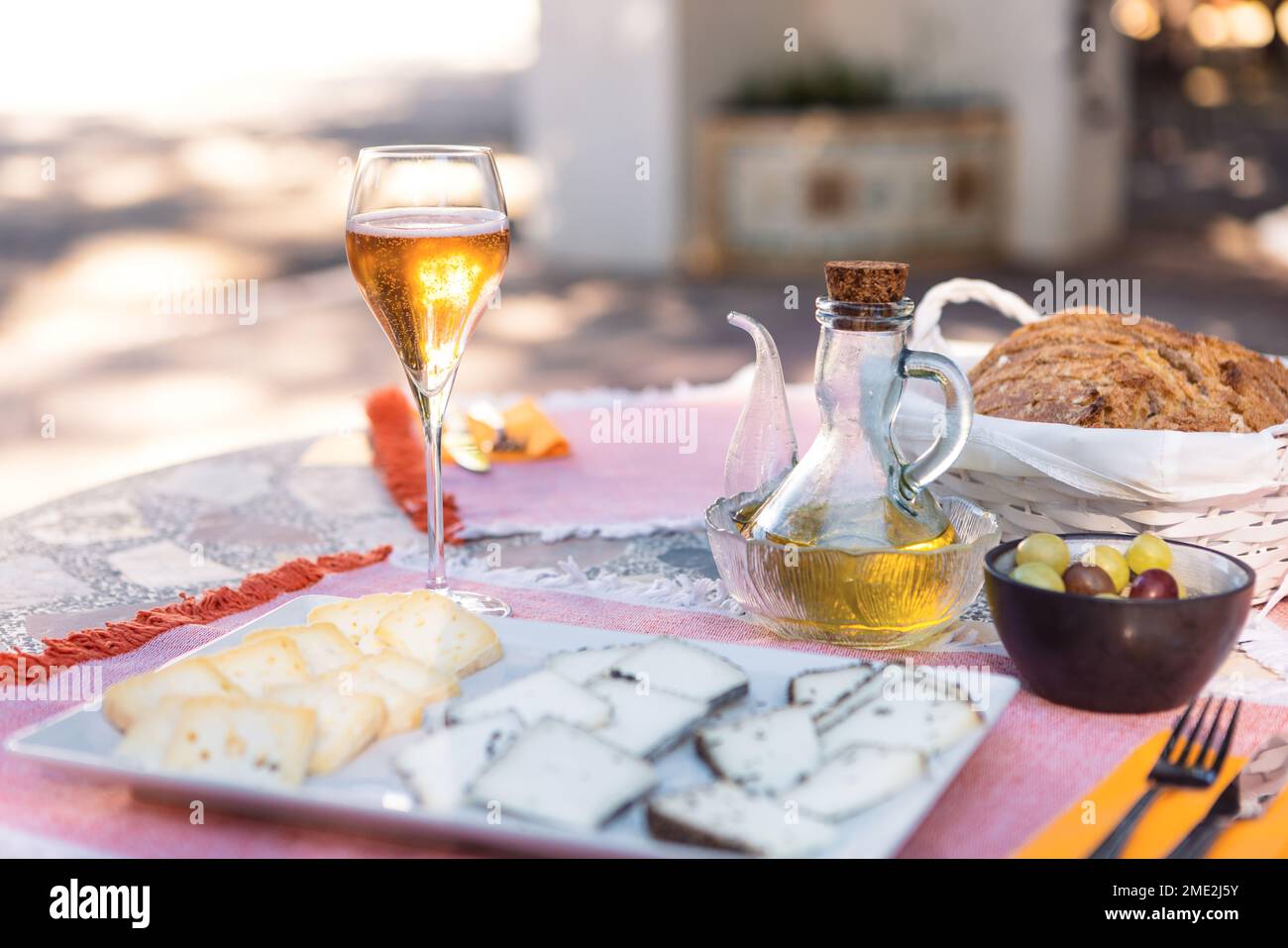 Auf der Außenterrasse bei Sonnenlicht wird eine Käseplatte mit hohem Winkel serviert, die mit Olivenöl und einem Glas kaltem Sekt serviert wird Stockfoto