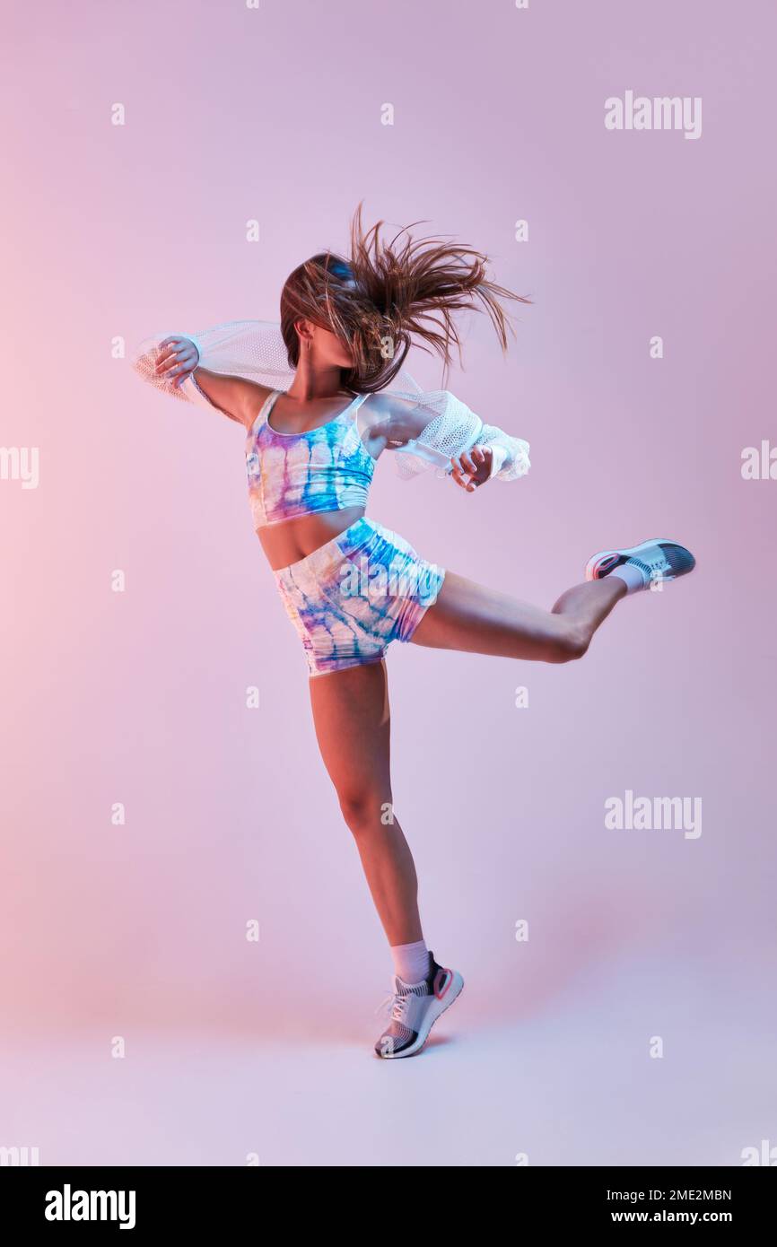 Junge schlanke Frau in enger Sportbekleidung hebt Arme und Beine, während sie im Studio vor pinkfarbenem Hintergrund tanzt Stockfoto