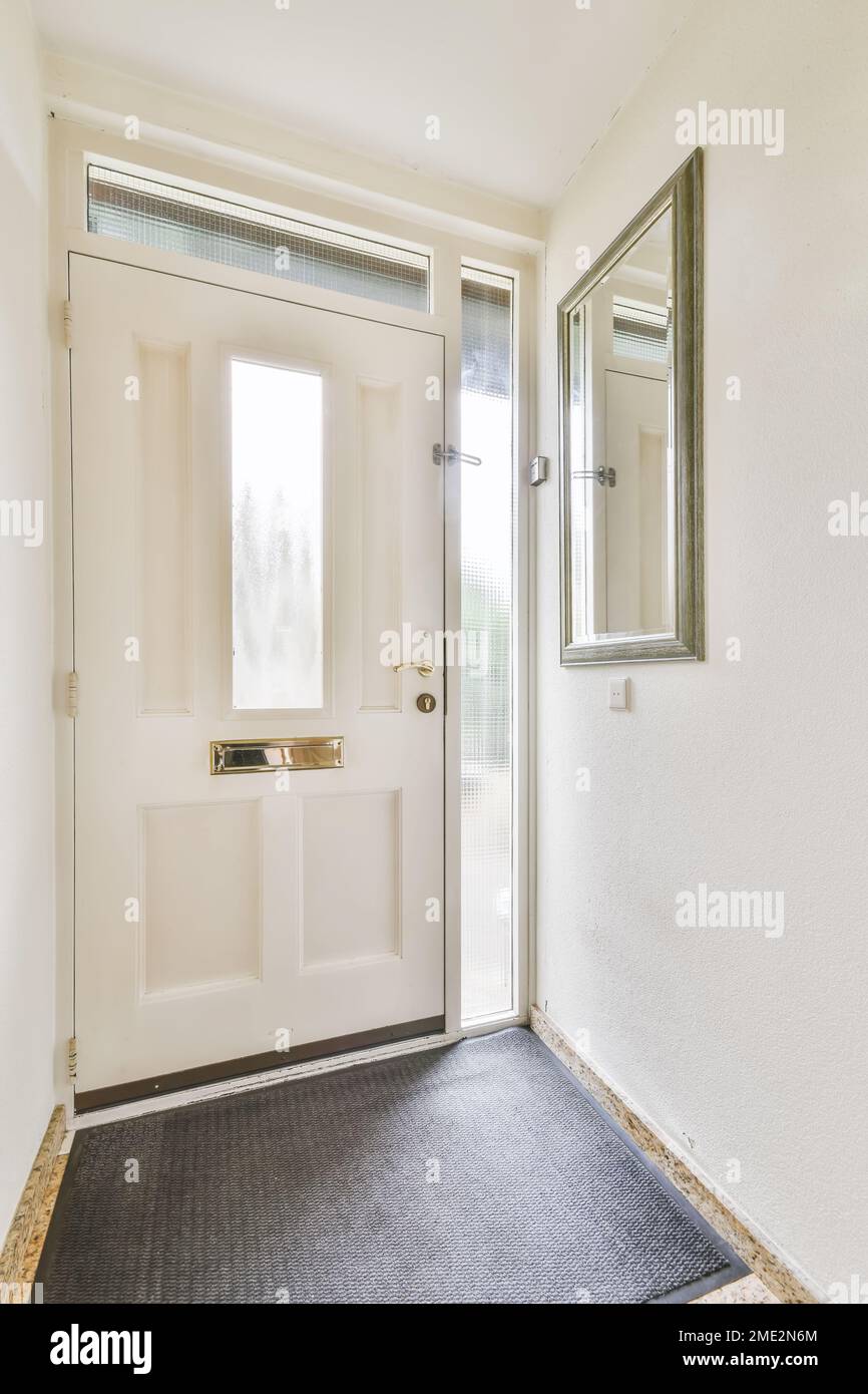 Innendesign eines kleinen Flurs mit weißer, großer Vordertür mit rechteckigem Fenster in der Mitte und Spiegel an der Wand Stockfoto