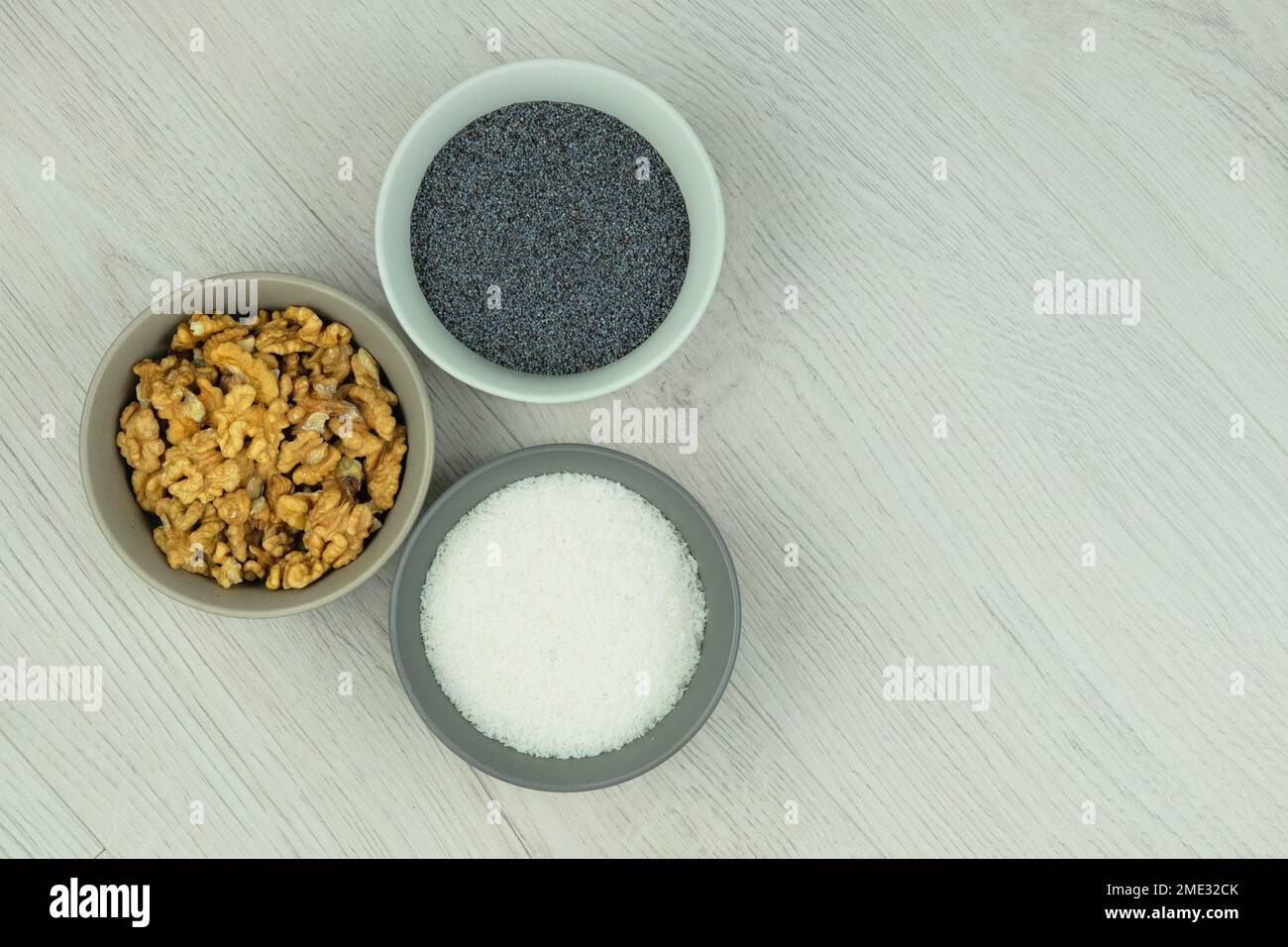 Mohnsamen, Kokosspäne und Walnüsse in Schüsseln auf holzigem Hintergrund. Zutaten, die zum Backen hinzugefügt werden können. Vegetarisches Produkt. Draufsicht. Speicherplatz kopieren. Stockfoto