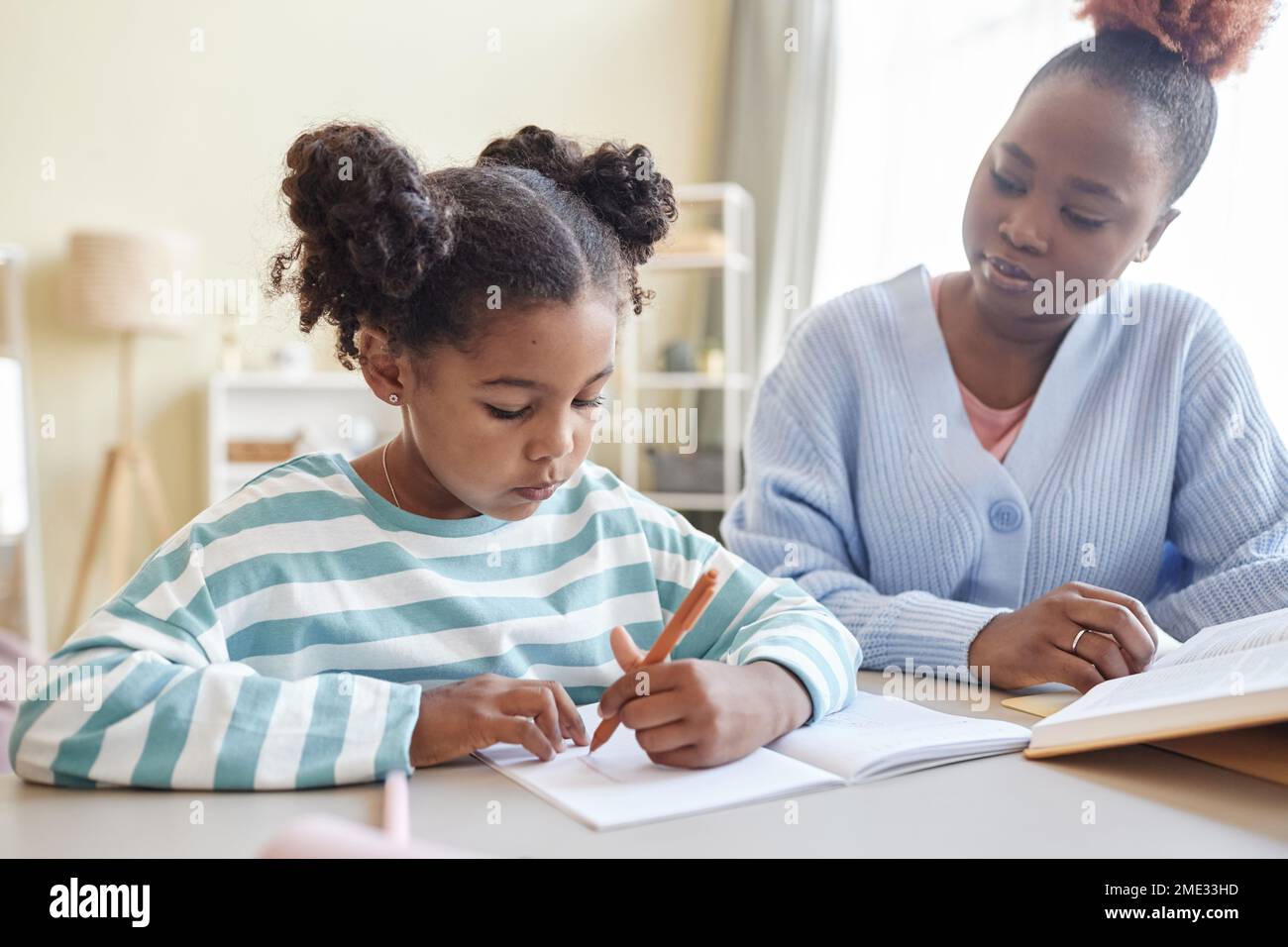 Porträt eines süßen schwarzen Mädchens, das zu Hause lernt, mit Hilfe einer fürsorglichen Mutter oder eines Betreuers Stockfoto