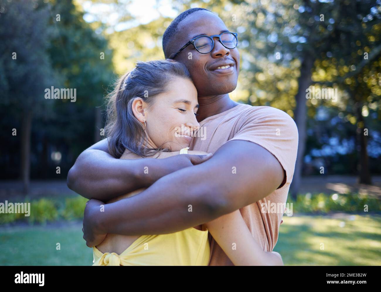 Schwarzer Mann, gemischtrassiges Paar und Umarmung auf dem Park Rasen mit Liebe, Sorgfalt und Verbundenheit für eine schöne Zeit, Wiedersehensfeier und Glück. Multikulturelle Umarmung, glücklich Stockfoto