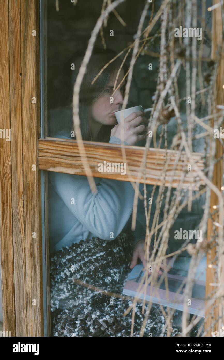 Eine Frau, die hinter einer Fensterscheibe Tee trinkt Stockfoto