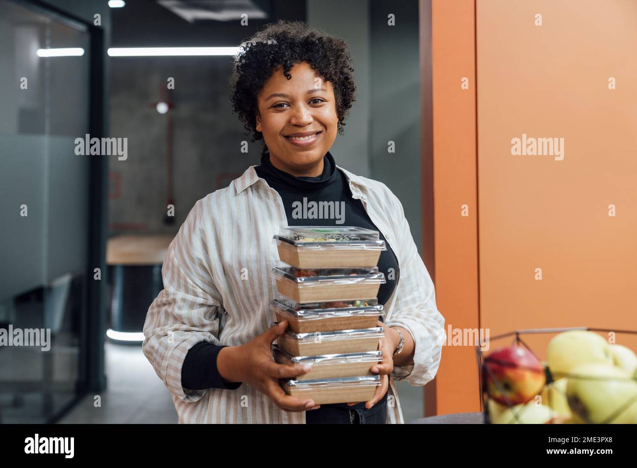 Glückliche junge Frau mit Essensboxen zum Mitnehmen im Büro Stockfoto