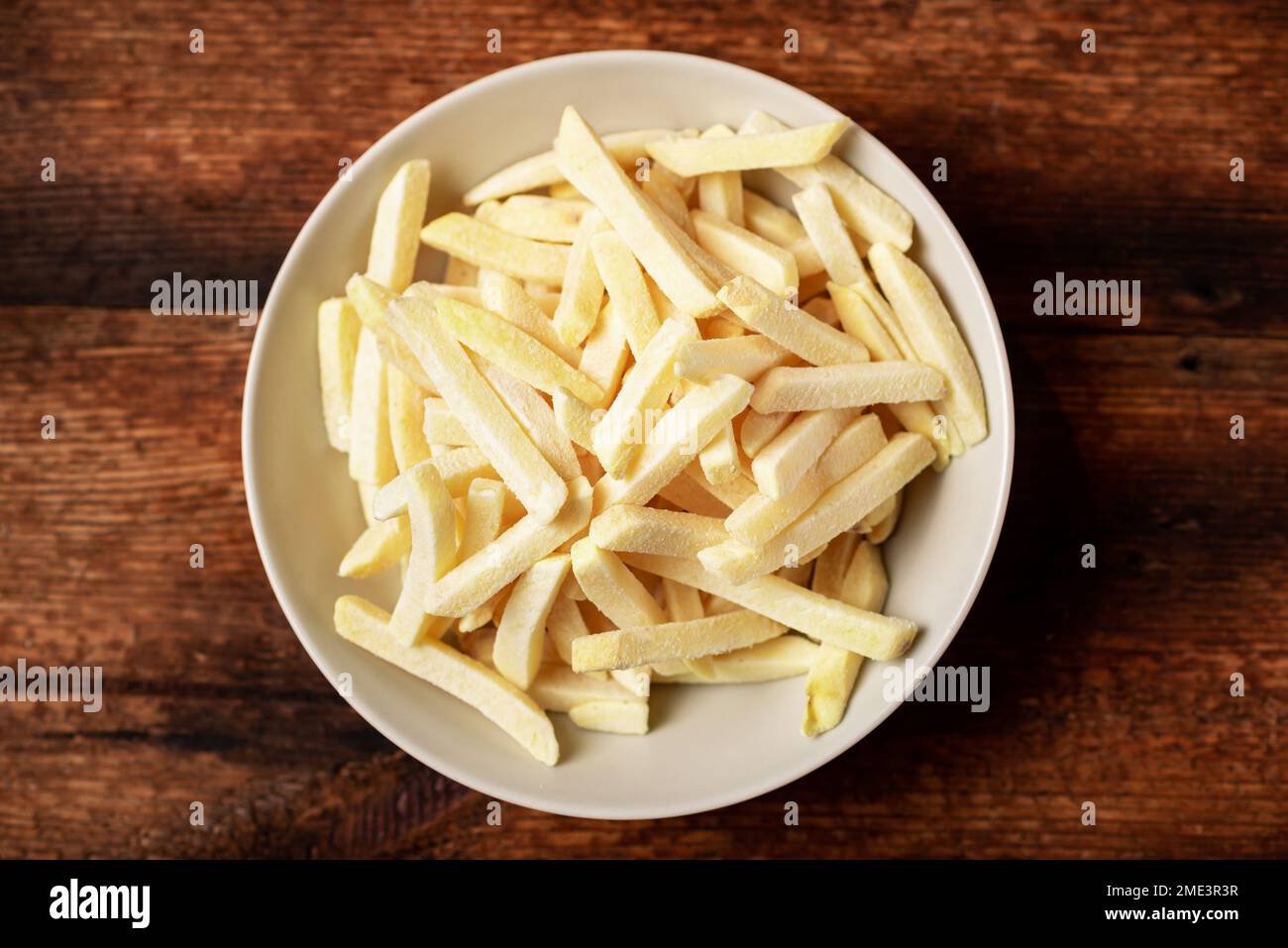 Gefrorene pommes frites auf einem Teller auf Holzhintergrund. Halbfertigerzeugnis aus gefrorenen Kartoffeln. Stockfoto
