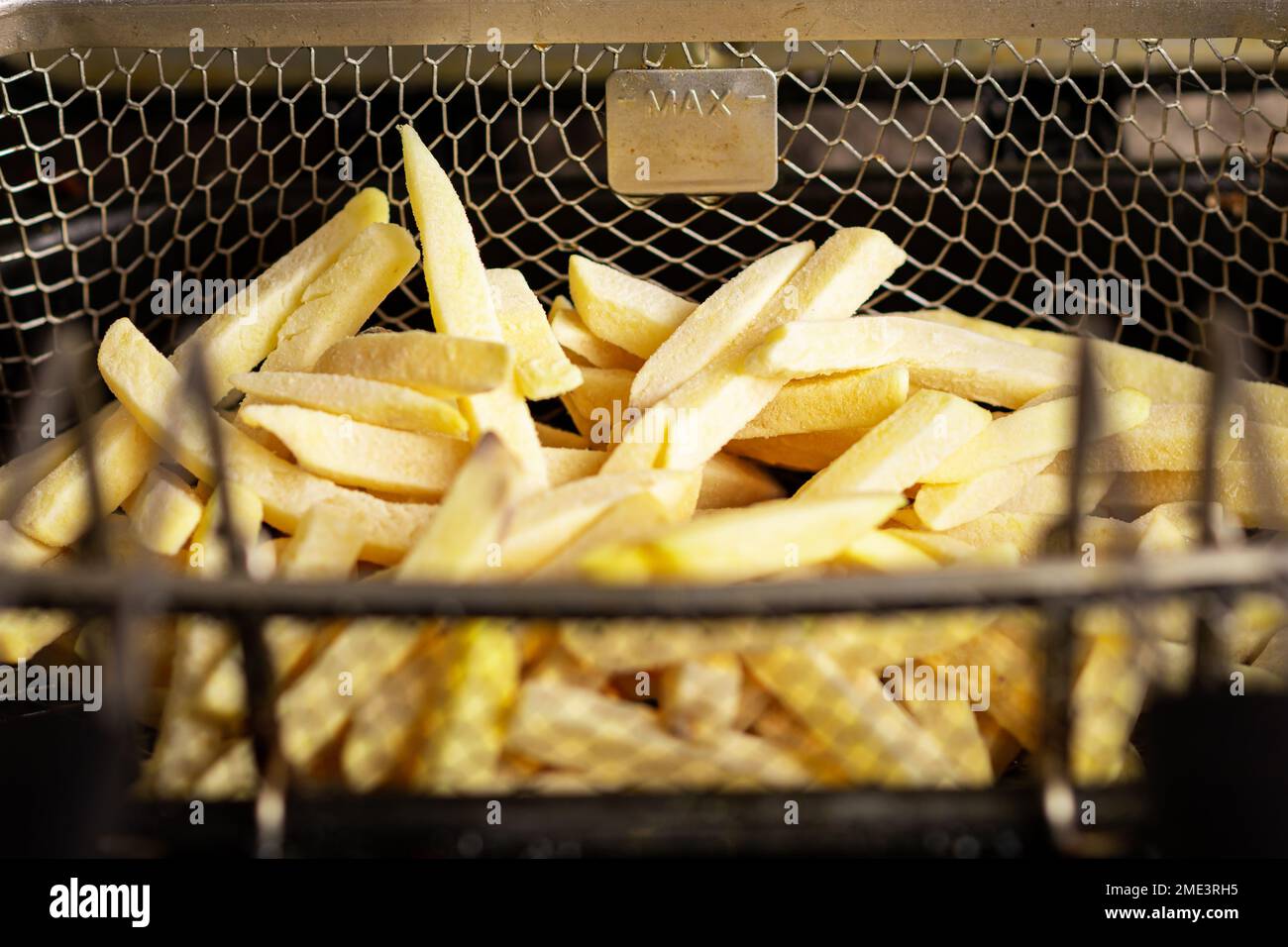 Gefrorene pommes frites in einem Friteusskorb. Halbfertigerzeugnis aus gefrorenen Kartoffeln. Zum Frittieren vorbereiten. Stockfoto
