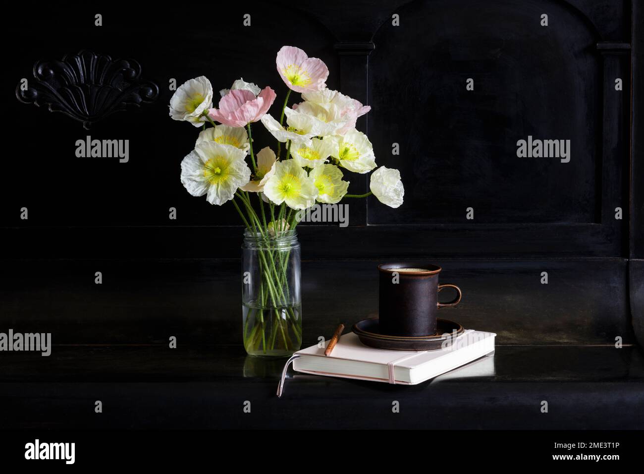 Isländische Mohnblumen in Glasgefäß, Kaffeetasse und Tagebuch auf schwarzem Klavier Stockfoto