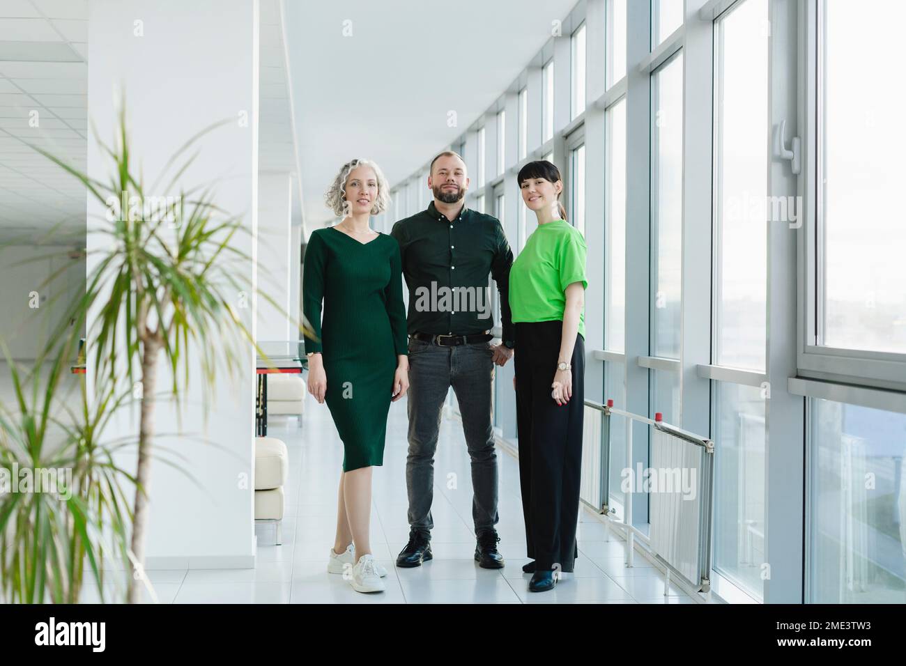 Drei Geschäftsleute in grüner Kleidung stehen auf dem Büroboden Stockfoto