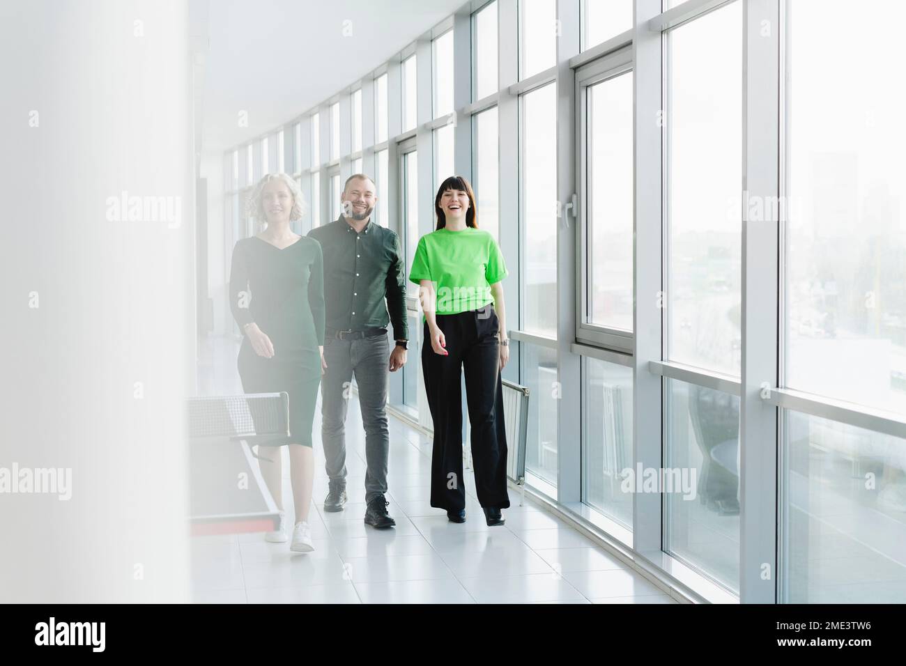 Drei glückliche Geschäftsleute in grüner Kleidung, die auf dem Büroboden herumlaufen Stockfoto