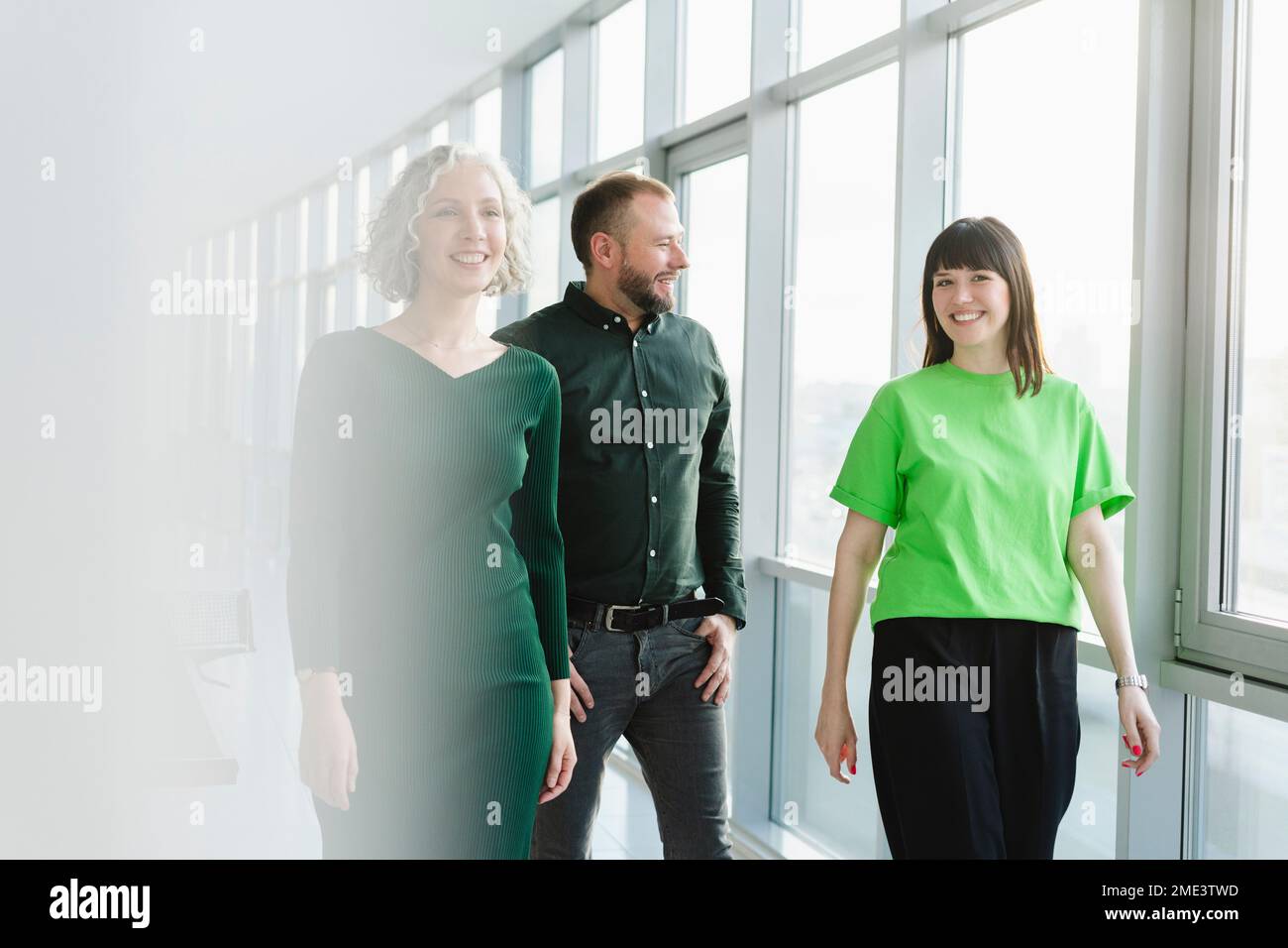 Drei glückliche Geschäftsleute in grüner Kleidung, die auf dem Büroboden herumlaufen Stockfoto