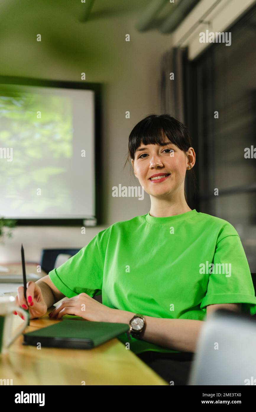 Lächelnde Frau mit grünem T-Shirt, die im Konferenzraum sitzt Stockfoto
