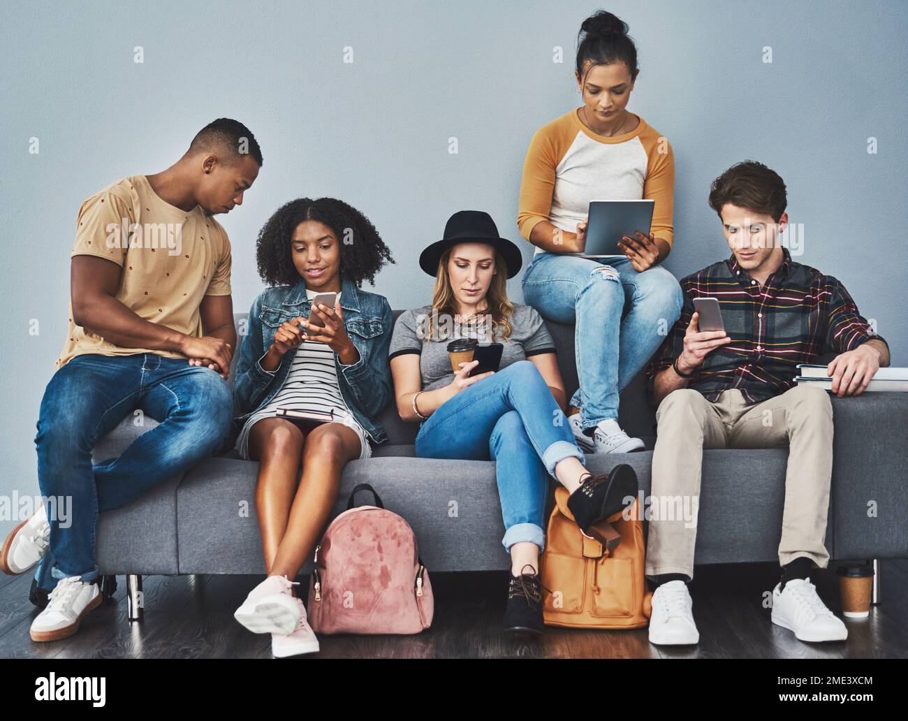 Keine Gruppe von Menschen ist besser in sozialen Medien als Millennials. Studiofoto von jungen Leuten, die auf einem Sofa sitzen und Wireless-Technologie gegen A verwenden Stockfoto