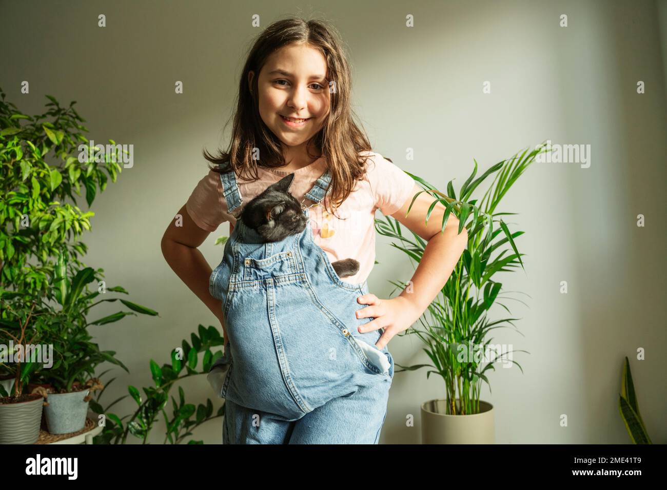 Lächelndes, süßes Mädchen mit Katze, die zu Hause vor der Wand steht Stockfoto