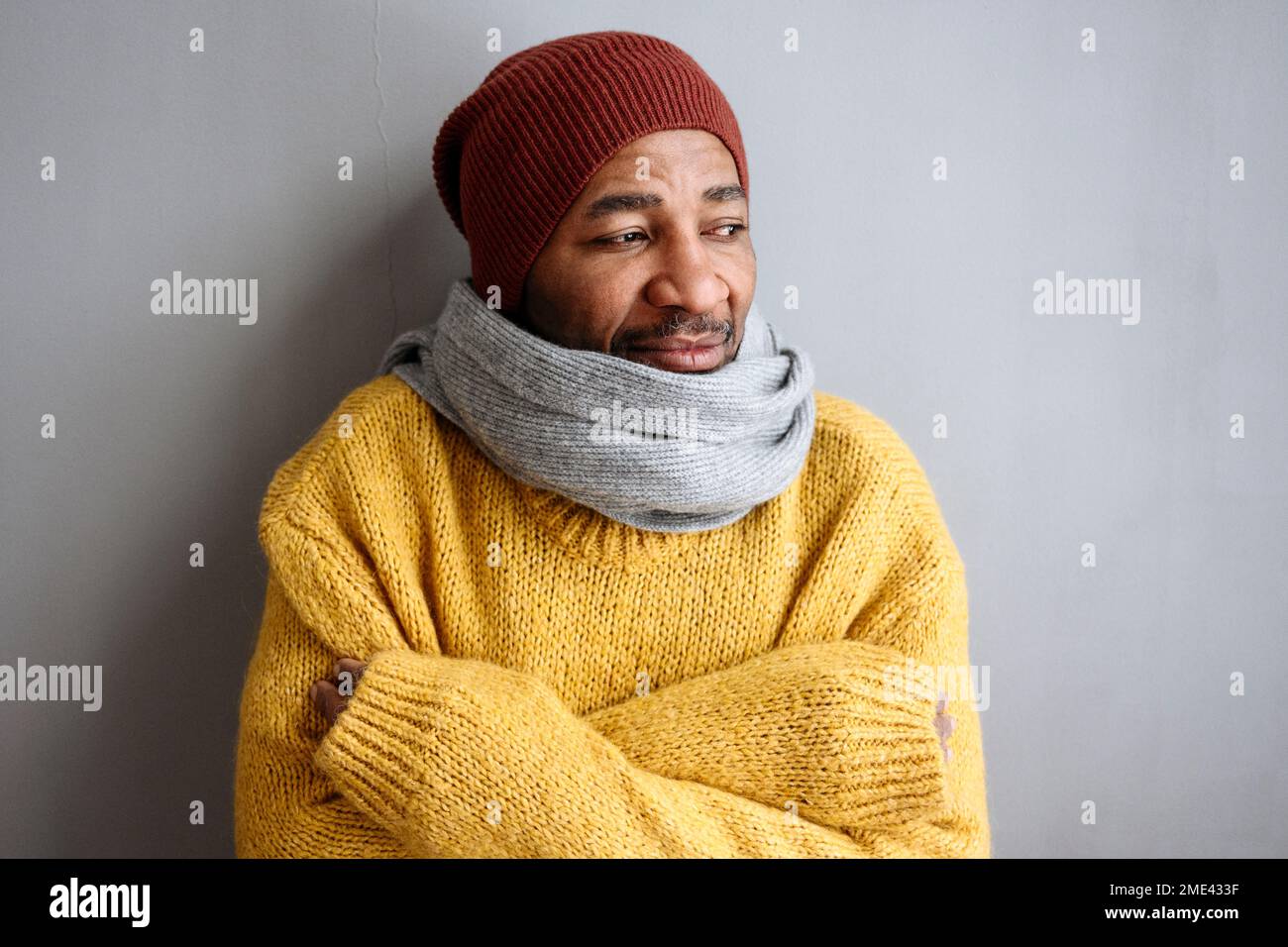 Ein erwachsener Mann, der warme Kleidung trägt und sich an eine graue Wand lehnt Stockfoto