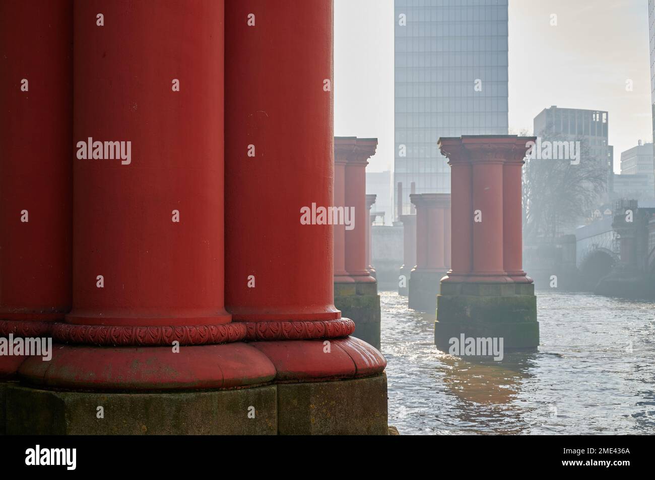 Muster aus roten Säulen oder Säulen von der ursprünglichen Blackfriars Eisenbahnbrücke in der Themse, london, an trüben sonnigen Wintertagen mit hohen Gebäuden Stockfoto