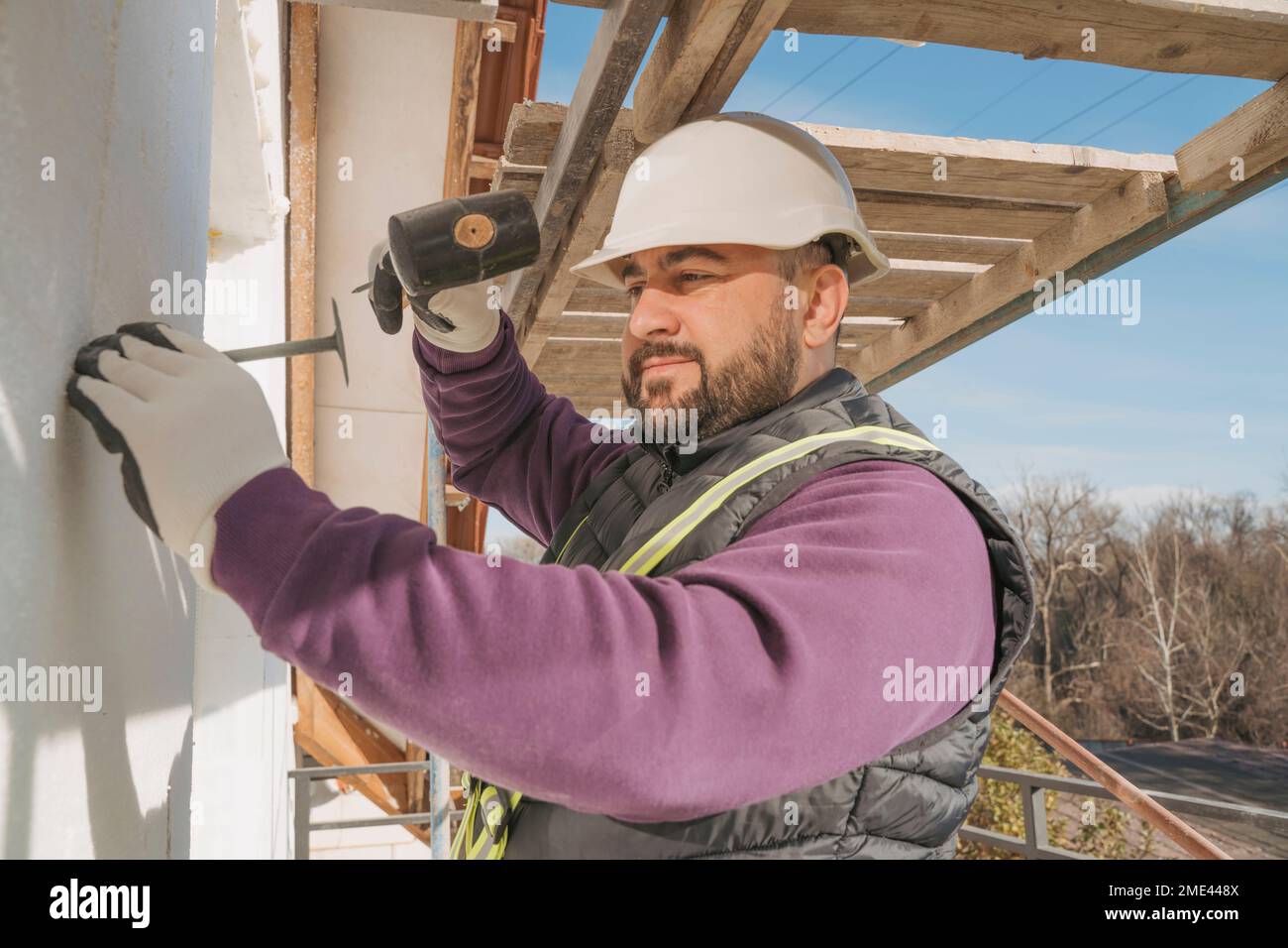 Bauarbeiter mit einem Hammer an der Wand, um Polystyrolschaum zu installieren Stockfoto