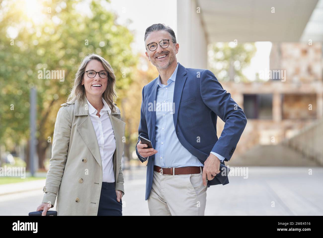 Fröhliche Geschäftsfrau und Geschäftsmann mit Smartphone, das auf dem Fußweg steht Stockfoto