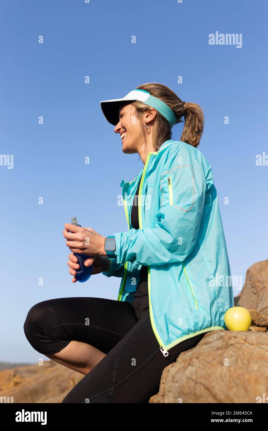 Glückliche Frau mit Wasserflasche, die auf einem Stein sitzt Stockfoto