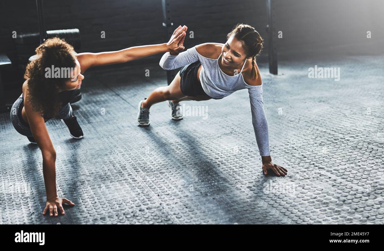 Teamwork macht das Workout zum Erfolg. Zwei junge Frauen, die sich gegenseitig High Five geben, während sie Liegestütze im Fitnessstudio machen. Stockfoto