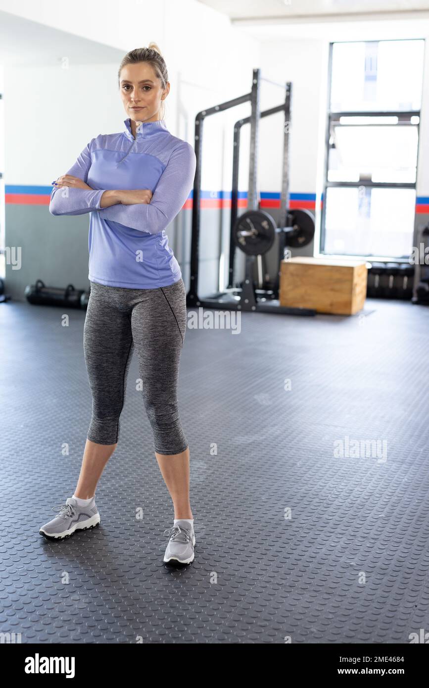 Porträt einer selbstbewussten, kaukasischen Frau mit gekreuzten Armen im Fitnessstudio, vertikales Bild mit Kopierbereich Stockfoto