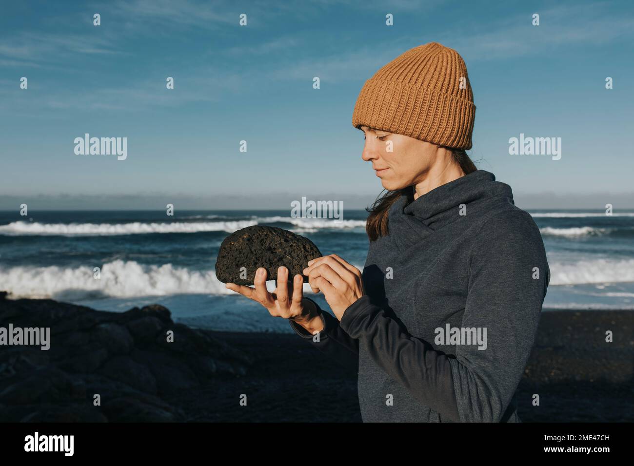 Frau mit Strickmütze, die auf Stein schaut, Janubio Beach, Lanzarote, Kanarische Inseln, Spanien Stockfoto