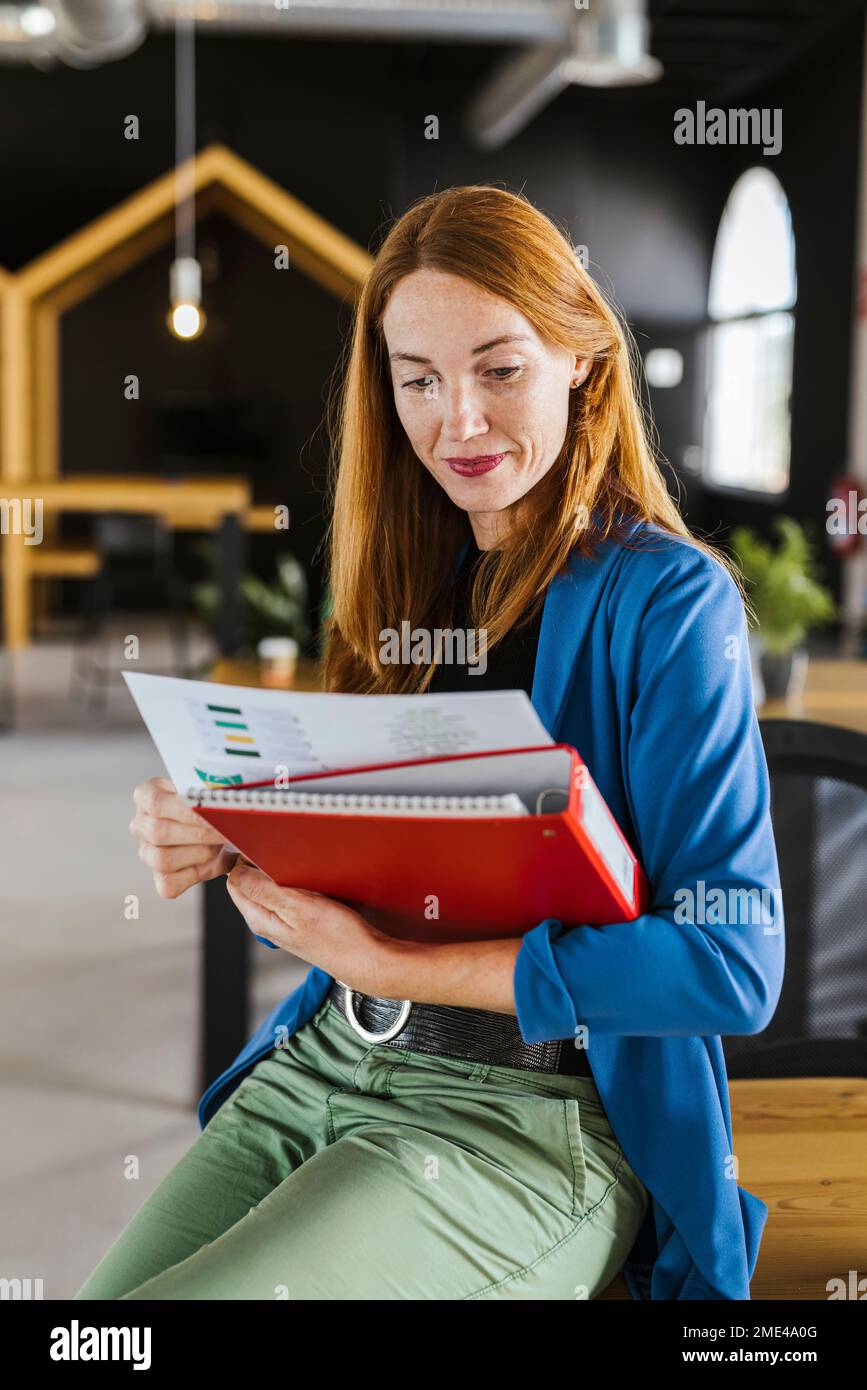 Lächelnde Geschäftsfrau mit Aktenordner und Dokumenten am Schreibtisch Stockfoto