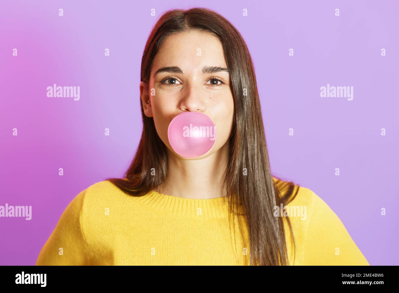 Junge Frau bläst Kaugummi vor violettem Hintergrund Stockfoto