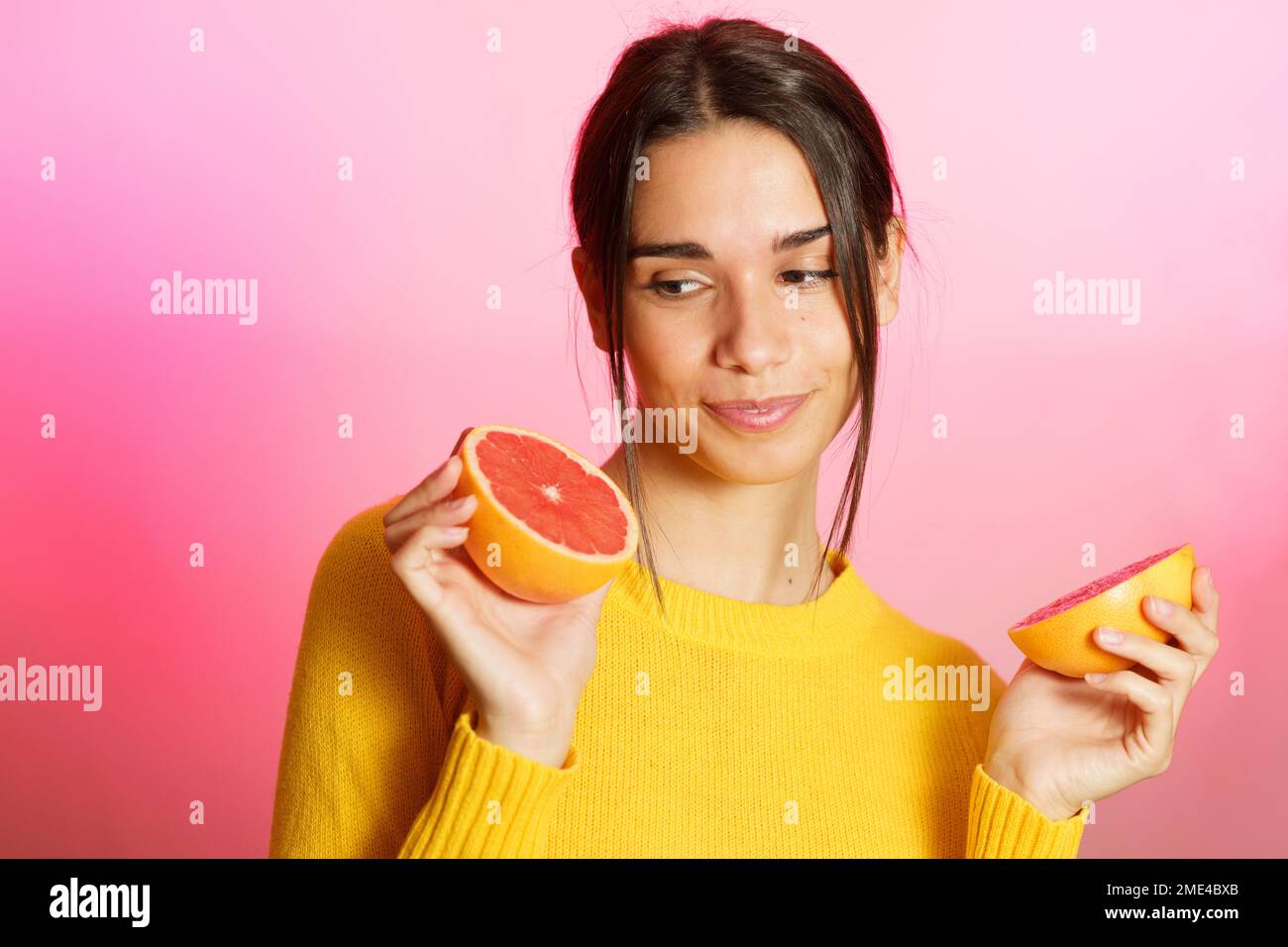 Lächelnde junge Frau mit Grapefruithälften vor pinkfarbenem Hintergrund Stockfoto