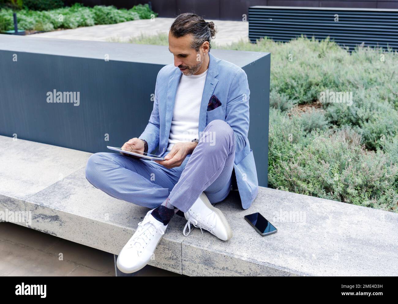 Ein erwachsener Mann, der einen Tablet-PC verwendet und auf einer Bank sitzt Stockfoto