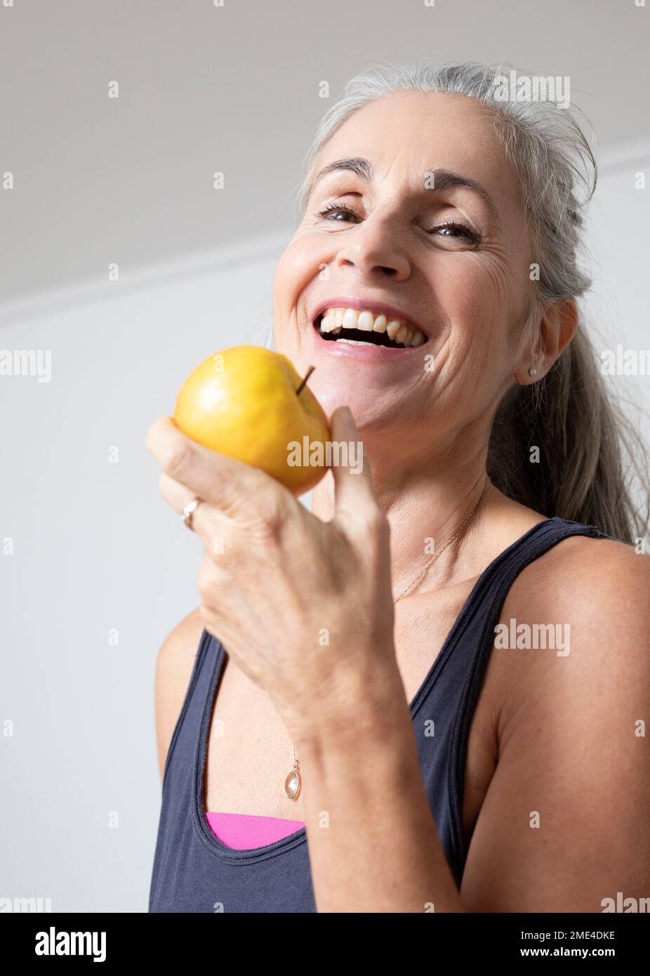 Glückliche reife Frau, die zu Hause Apfel isst Stockfoto