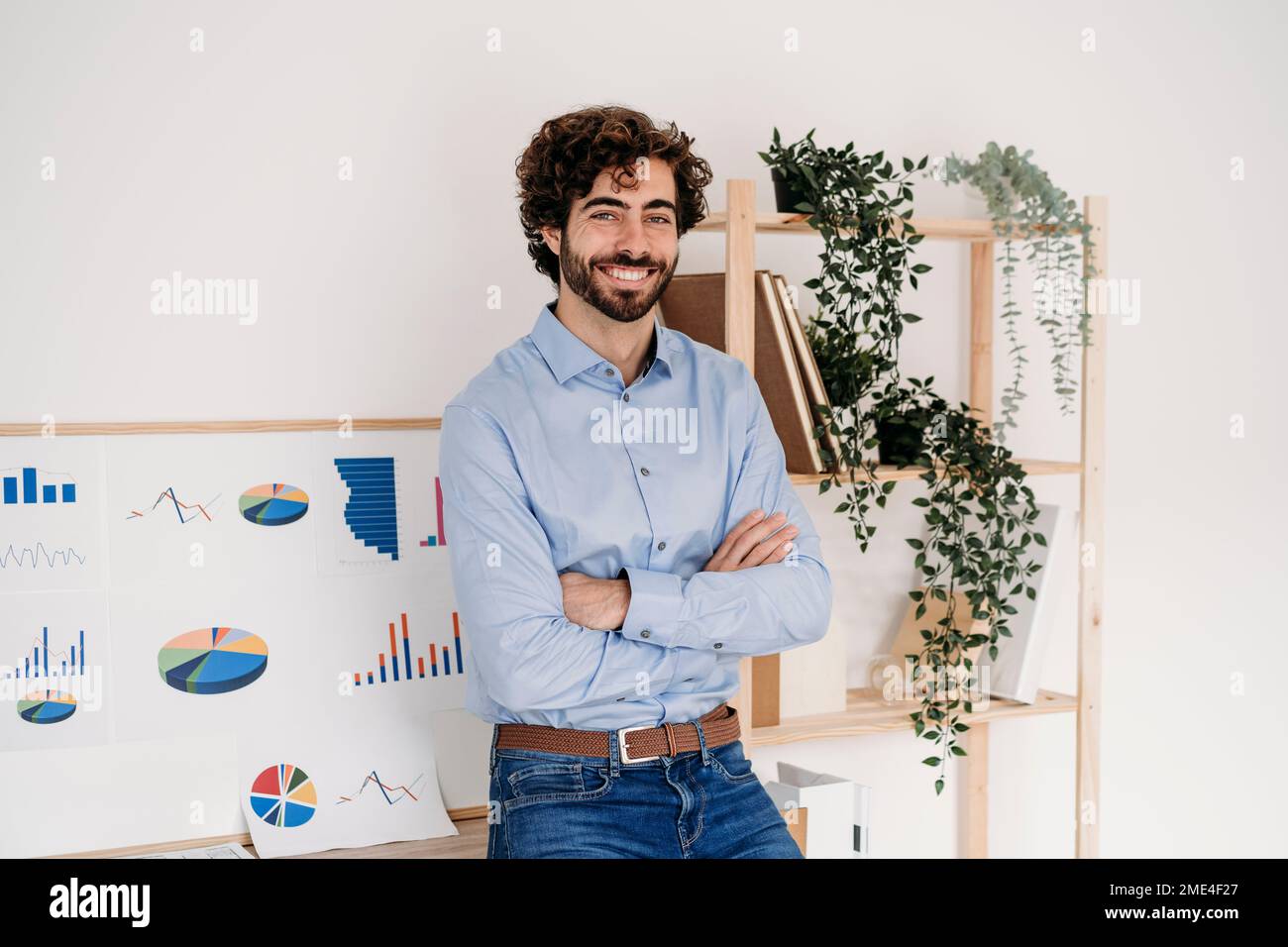 Ein fröhlicher junger Geschäftsmann mit gekreuzten Armen, der im Amt steht Stockfoto