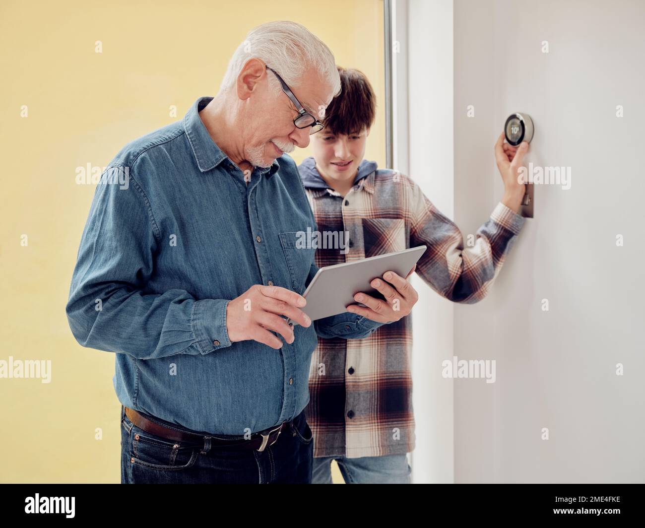 Großvater und Enkel, die zu Hause auf einem digitalen Tablet mit intelligentem Thermostat arbeiten Stockfoto