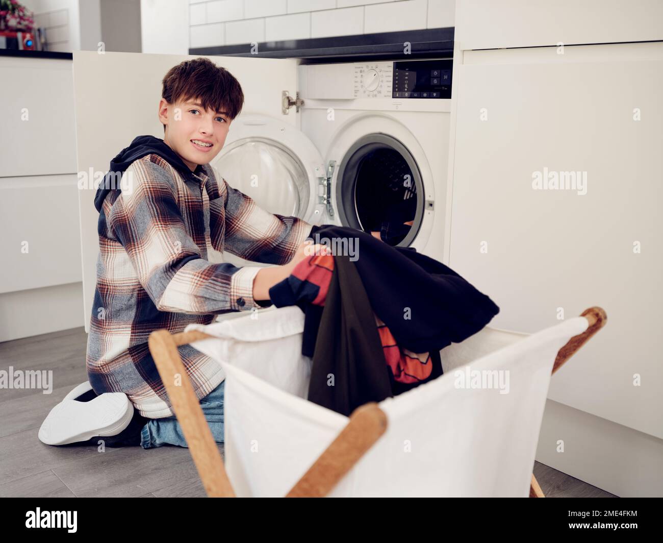 Lächelnder Junge, der zu Hause Wäsche in die Waschmaschine legt Stockfoto