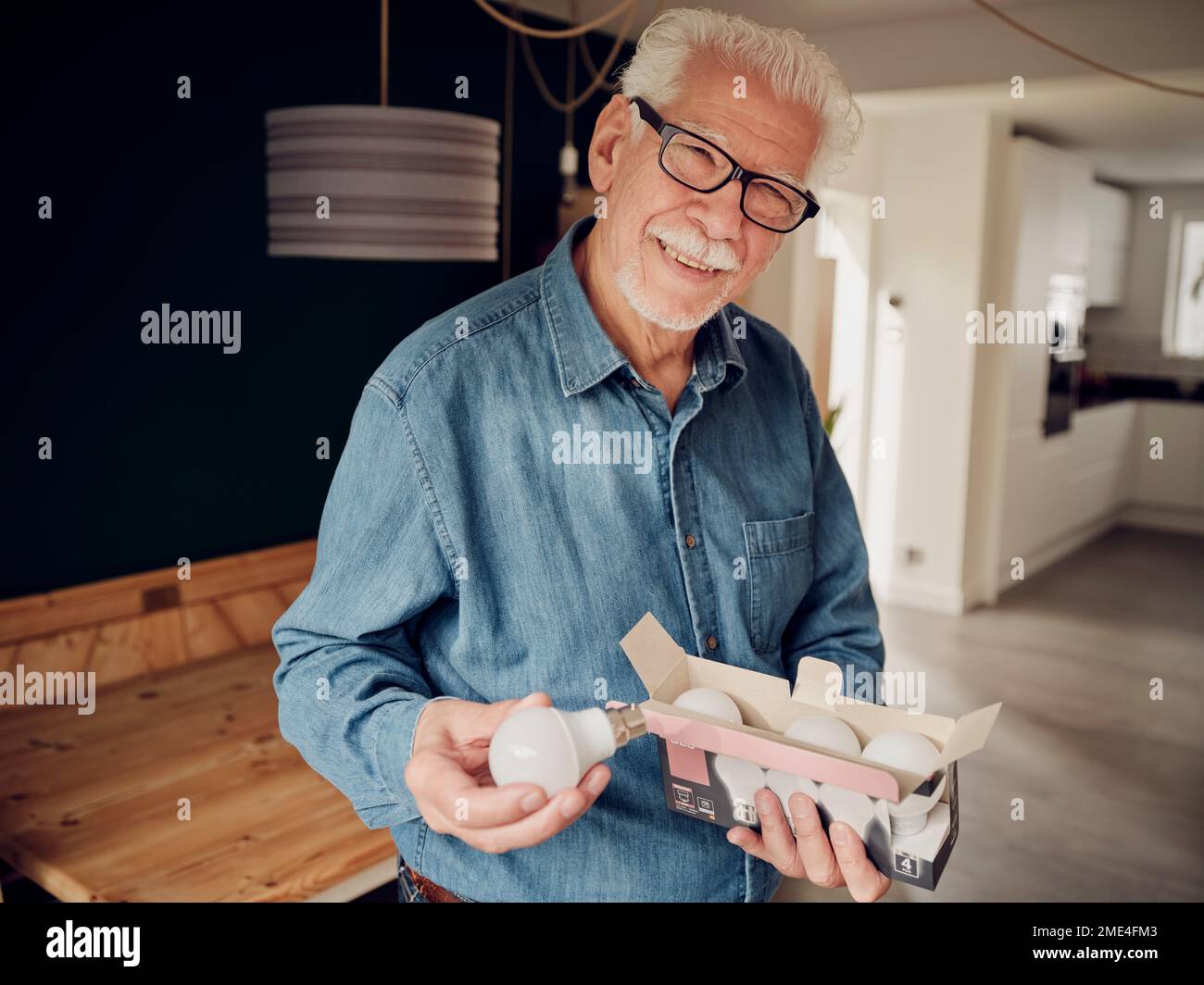 Ein älterer Mann, der zu Hause eine Schachtel LED-Glühbirnen in der Hand hat Stockfoto
