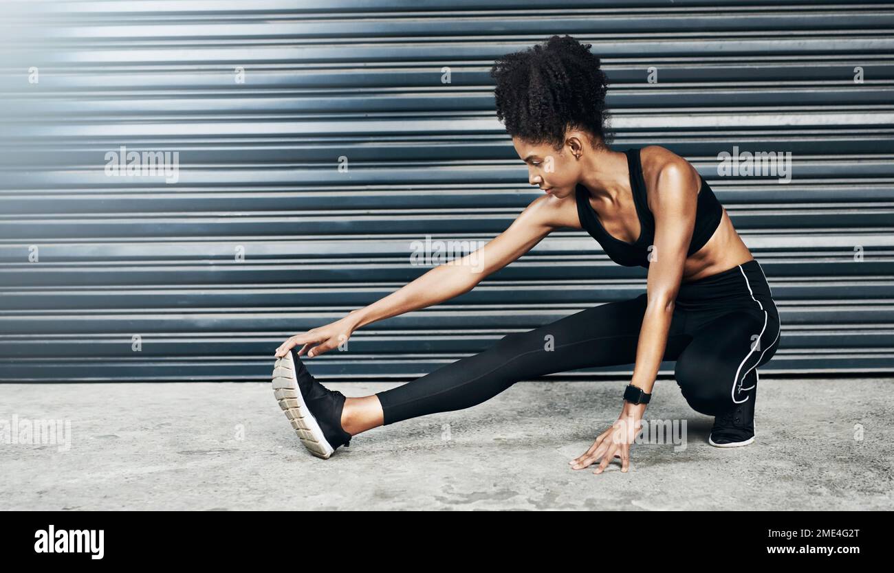 Ganz ruhig. Eine sportliche junge Frau, die sich vor grauem Hintergrund die Beine ausstreckt. Stockfoto