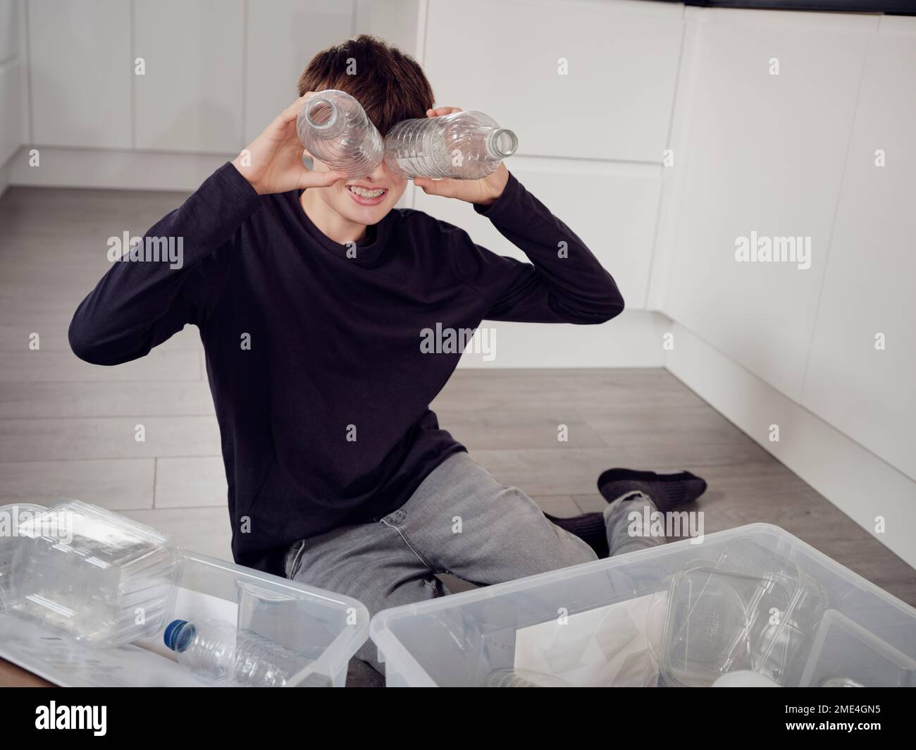 Ein Junge, der Plastikabfälle trennt und die Augen mit Plastikflaschen bedeckt Stockfoto